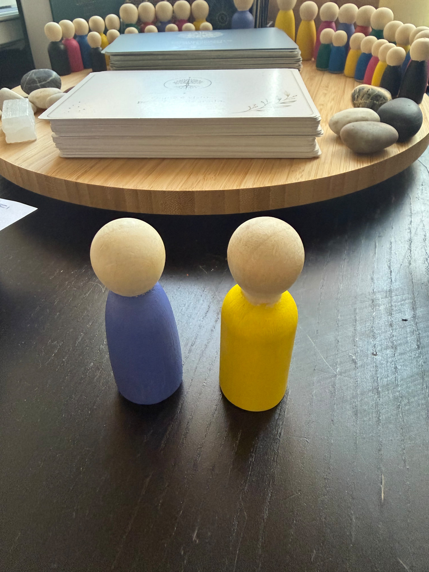 Duas figuras de madeira frente a frente, com outras figuras e cartas ao fundo